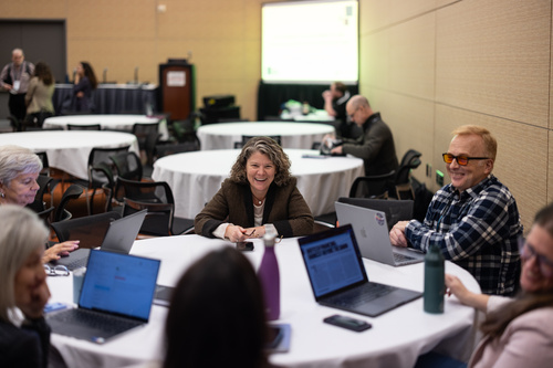Heidi Rehm sits at a table surrounded by other people at a presentation.