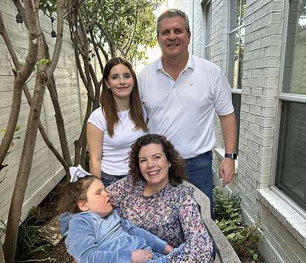 Four members of a family pose together for a portrait outdoors between two buildings.