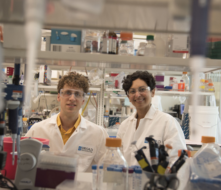 Erik Minikel and Sonia Vallabh stand side-by-side in a lab, wearing lab coats.