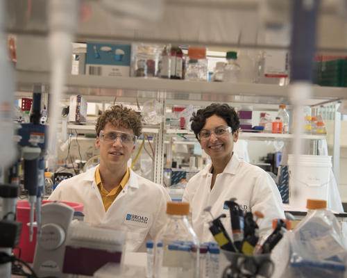 Erik Minikel and Sonia Vallabh stand side-by-side in a lab, wearing lab coats.