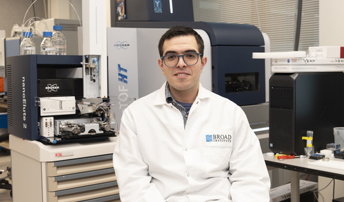 Moe Haines is sitting in a lab wearing a white lab coat. Behind him are various pieces of lab equipment.