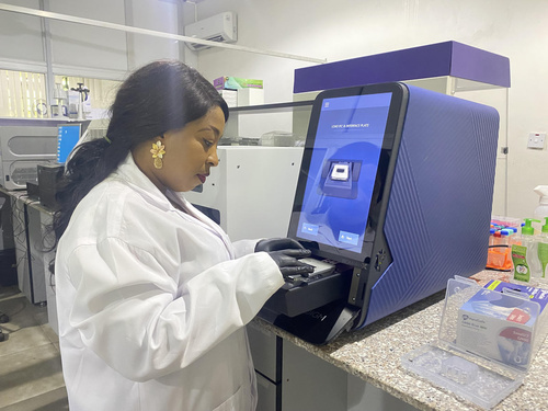 A scientist in a lab coat loads a plate of samples into an instrument in a lab.